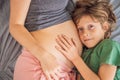 Young beautiful pregnant woman and eldest son. The cute boy leaned his ear against his mother& x27;s belly. Expecting a