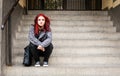 Young beautiful red hair girl sitting alone outdoors on the stairs of the building with hat and shirt feeling anxious and depresse Royalty Free Stock Photo