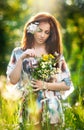 Young beautiful red hair woman holding a wild flowers bouquet in a sunny day. Portrait of attractive long hair female with flowers Royalty Free Stock Photo