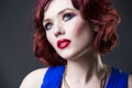 Young beautiful red-haired caucasian woman in blue dress posing in studio on gray background, professional makeup and hairstyle Royalty Free Stock Photo