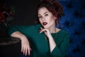 Young beautiful red-haired caucasian woman with professional makeup in green dress posing on blue sofa Royalty Free Stock Photo