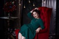 Young beautiful red-haired caucasian woman with professional makeup in green dress posing on red sofa Royalty Free Stock Photo