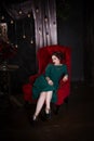 Young beautiful red-haired caucasian woman with professional makeup in green dress posing on red sofa Royalty Free Stock Photo