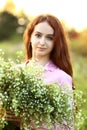 A young beautiful red-haired girl close-up is looking at the camera with a huge bouquet of field daisies in a pink dress. Sunset Royalty Free Stock Photo