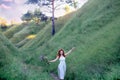 A young beautiful red-haired girl in a green sundress in the summer walks where the hills and mountains, green grass and