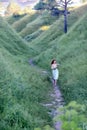 A young beautiful red-haired girl in a green sundress in the summer walks where the hills and mountains, green grass and