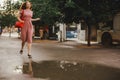 Young beautiful red-haired long-haired woman in a summer pink dress walks through the streets of a summer city. Royalty Free Stock Photo