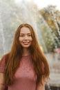 Young beautiful red-haired long-haired woman in a summer pink dress walks through the streets of a summer city. Royalty Free Stock Photo