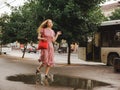 Young beautiful red-haired long-haired woman in a summer pink dress walks through the streets of a summer city. Royalty Free Stock Photo