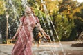 Young beautiful red-haired long-haired woman in a summer pink dress walks through the streets of a summer city. Royalty Free Stock Photo