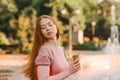 Young beautiful red-haired long-haired woman in a summer pink dress walks through the streets of a summer city. Royalty Free Stock Photo