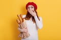 Young beautiful red haired woman wearing french beret, holding bread, covering mouth with hand, has surprised expression, looks at Royalty Free Stock Photo