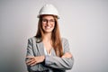 Young beautiful redhead architect woman wearing security helmet over white background happy face smiling with crossed arms looking Royalty Free Stock Photo