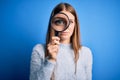 Young beautiful redhead detective woman using magnifying glass over blue background with a confident expression on smart