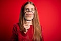 Young beautiful redhead detective woman using magnifying glass over isolated red background with a confident expression on smart