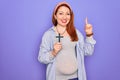 Young beautiful redhead pregnant woman expecting baby holding christian cross surprised with an idea or question pointing finger