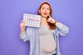 Young beautiful redhead pregnant woman expecting baby holding period calendar serious face thinking about question, very confused Royalty Free Stock Photo