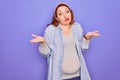 Young beautiful redhead pregnant woman expecting baby over isolated purple background clueless and confused expression with arms Royalty Free Stock Photo