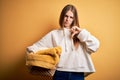 Young beautiful redhead woman doing housework holding wicker basket with clothes with angry face, negative sign showing dislike