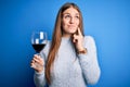 Young beautiful redhead woman drinking glass of red wine over isolated blue background serious face thinking about question, very Royalty Free Stock Photo