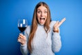 Young beautiful redhead woman drinking glass of red wine over isolated blue background very happy and excited, winner expression Royalty Free Stock Photo