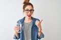 Young beautiful redhead woman drinking glass of water over isolated white background pointing and showing with thumb up to the Royalty Free Stock Photo