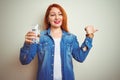 Young beautiful redhead woman drinking glass of water over white isolated background pointing and showing with thumb up to the Royalty Free Stock Photo