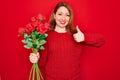 Young beautiful redhead woman holding bouquet of red roses flowers over isolated background happy with big smile doing ok sign, Royalty Free Stock Photo