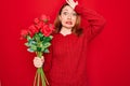 Young beautiful redhead woman holding bouquet of red roses flowers over isolated background stressed with hand on head, shocked Royalty Free Stock Photo