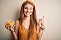 Young beautiful redhead woman holding bowl with potato chips over isolated white background happy with big smile doing ok sign, Royalty Free Stock Photo