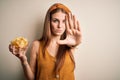 Young beautiful redhead woman holding bowl with potato chips over isolated white background with open hand doing stop sign with Royalty Free Stock Photo