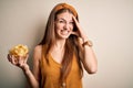 Young beautiful redhead woman holding bowl with potato chips over isolated white background stressed with hand on head, shocked Royalty Free Stock Photo