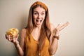 Young beautiful redhead woman holding bowl with potato chips over isolated white background very happy and excited, winner Royalty Free Stock Photo