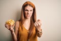 Young beautiful redhead woman holding bowl with potato chips over  white background annoyed and frustrated shouting with Royalty Free Stock Photo