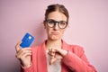 Young beautiful redhead woman holding credit card over isolated pink background with angry face, negative sign showing dislike Royalty Free Stock Photo