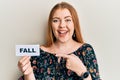 Young beautiful redhead woman holding fall word on paper smiling happy pointing with hand and finger