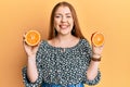 Young beautiful redhead woman holding fresh orange slices smiling with a happy and cool smile on face Royalty Free Stock Photo