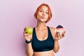 Young beautiful redhead woman holding green apple and cake slice looking at the camera blowing a kiss being lovely and sexy Royalty Free Stock Photo