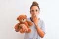 Young beautiful redhead woman holding stuffed teddy bear over isolated background cover mouth with hand shocked with shame for Royalty Free Stock Photo