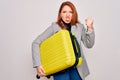 Young beautiful redhead woman holding suitcase prepared to business travel annoyed and frustrated shouting with anger, crazy and Royalty Free Stock Photo