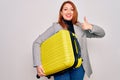 Young beautiful redhead woman holding suitcase prepared to business travel happy with big smile doing ok sign, thumb up with Royalty Free Stock Photo