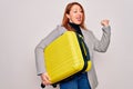 Young beautiful redhead woman holding suitcase prepared to business travel pointing and showing with thumb up to the side with Royalty Free Stock Photo