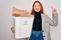 Young beautiful redhead woman recycling holding trash can with cardboard to recycle surprised with an idea or question pointing Royalty Free Stock Photo