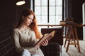 Young beautiful redhead woman relaxing at home in the autumn cozy evening and reading book Royalty Free Stock Photo