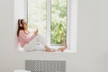 Young beautiful redhead woman sitting on windowsill and listening music in headphones. Royalty Free Stock Photo