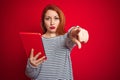 Young beautiful redhead woman using tablet over red isolated background pointing with finger to the camera and to you, hand sign, Royalty Free Stock Photo