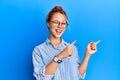 Young beautiful redhead woman wearing casual clothes and glasses over blue background smiling and looking at the camera pointing Royalty Free Stock Photo