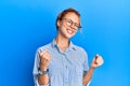 Young beautiful redhead woman wearing casual clothes and glasses over blue background very happy and excited doing winner gesture Royalty Free Stock Photo