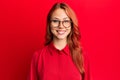 Young beautiful redhead woman wearing casual clothes and glasses over red background with a happy and cool smile on face Royalty Free Stock Photo