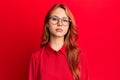 Young beautiful redhead woman wearing casual clothes and glasses over red background relaxed with serious expression on face Royalty Free Stock Photo